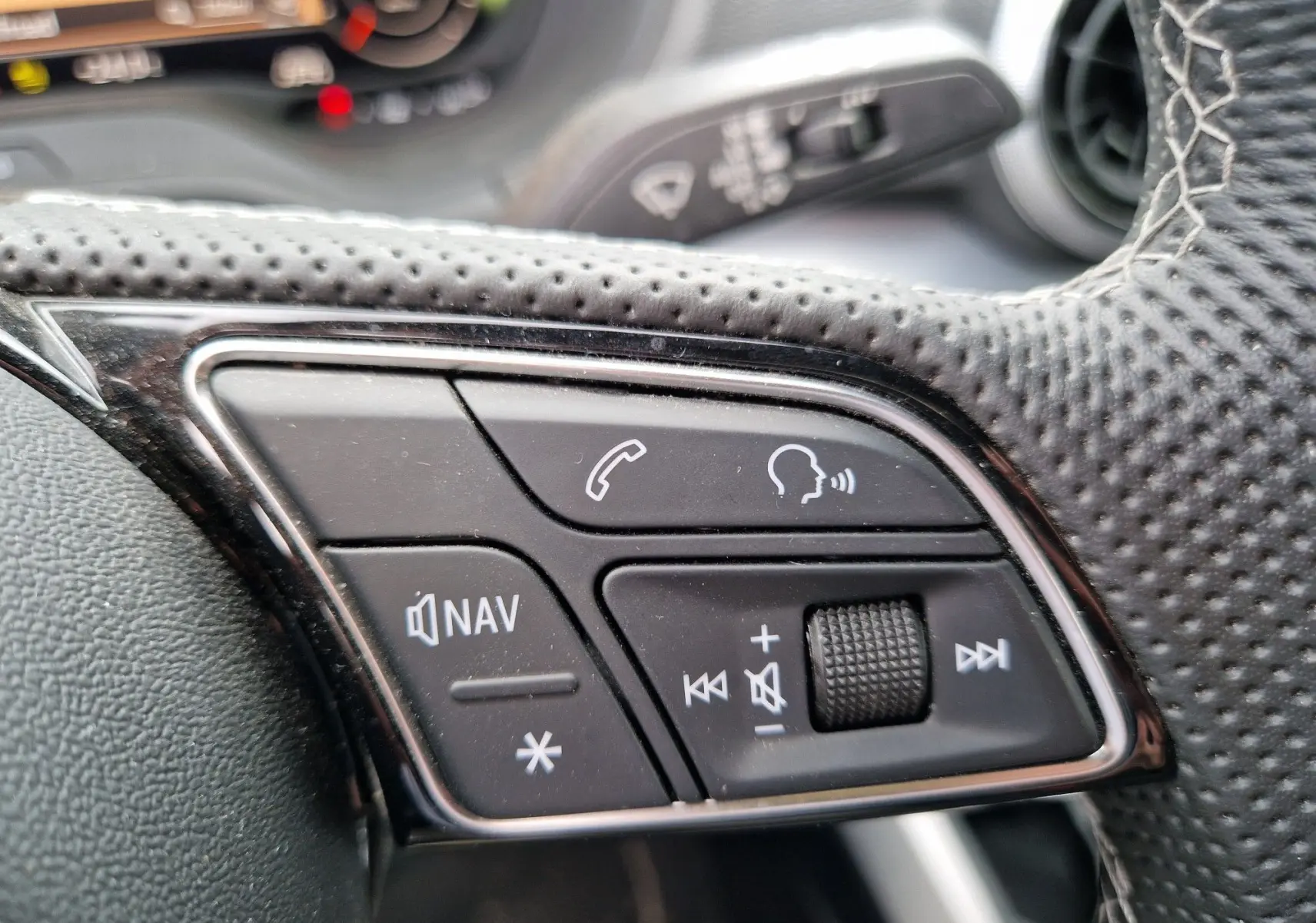 Gros plan sur les commandes multifonctions au volant perforé de l’Audi Q2 35 TFSI gris flèche, finition S line.