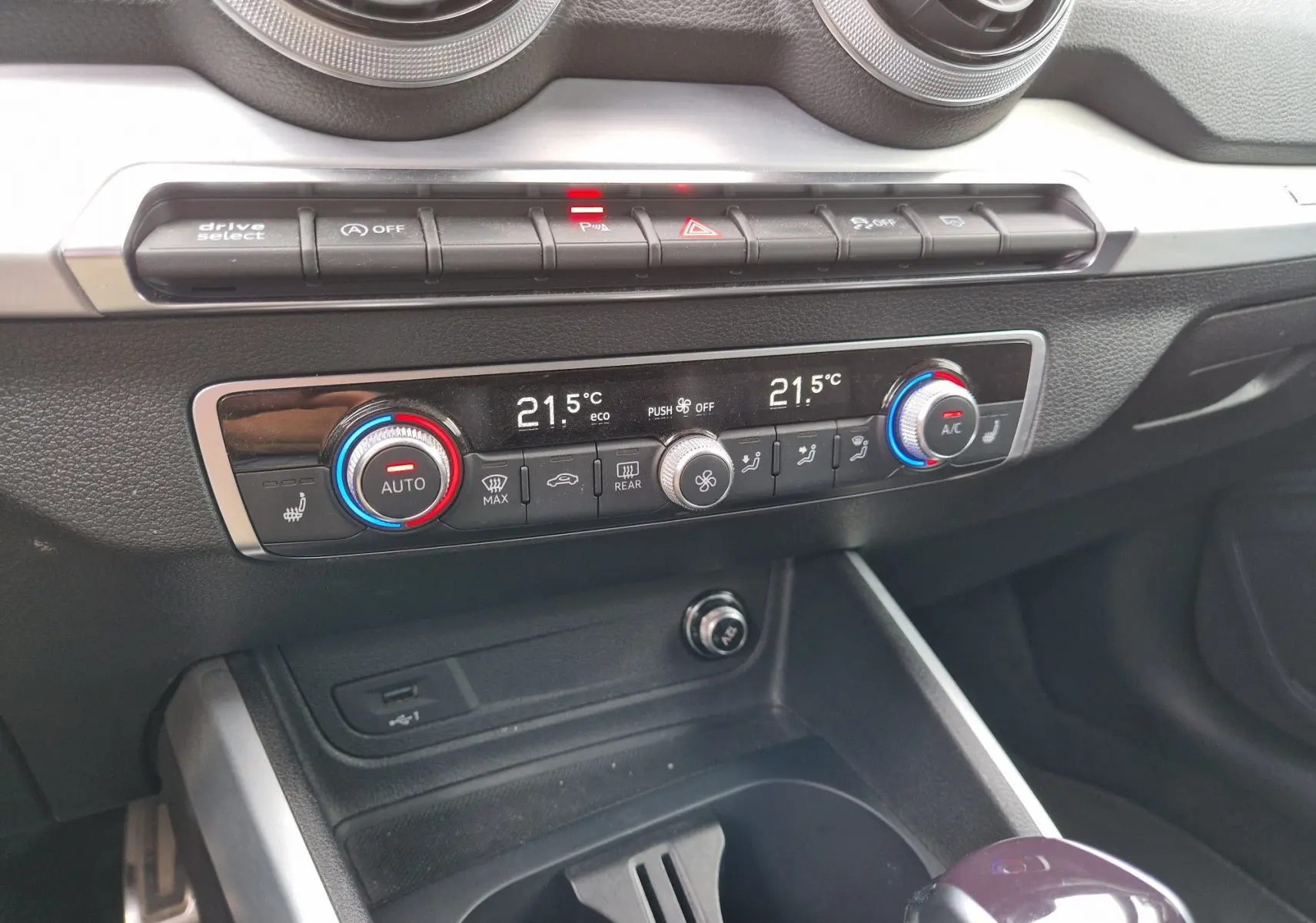 Vue rapprochée du tableau de bord de l'Audi Q2 35 TFSI 2023, montrant la climatisation automatique et les commandes en aluminium brossé.