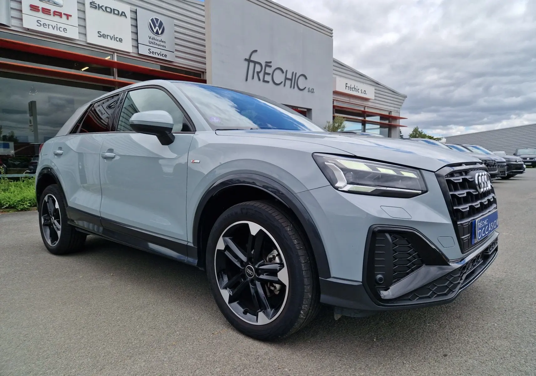 Audi Q2 35 TFSI 2023 gris flèche vue 3/4 avant droit, finition S line avec jantes sport 18 pouces noires.
