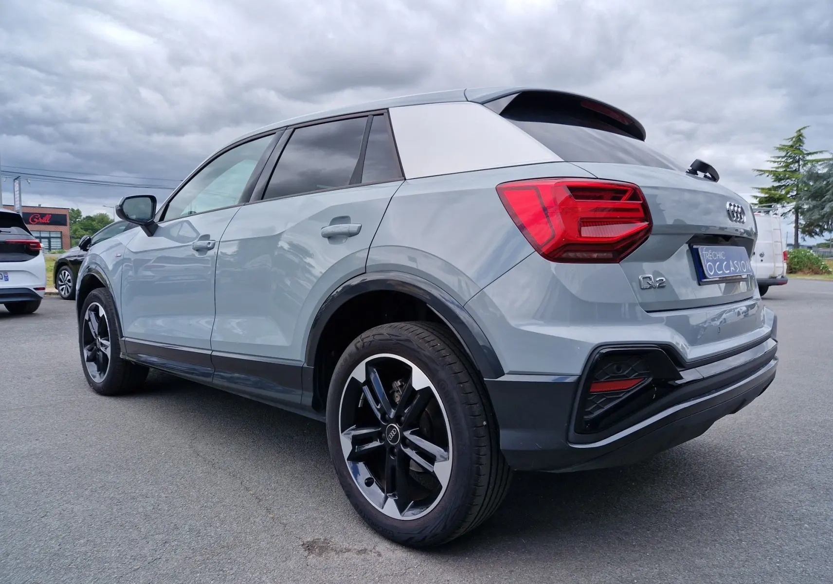 Audi Q2 gris flèche en vue 3/4 arrière droit, avec jantes sport 18 pouces et vitres teintées.