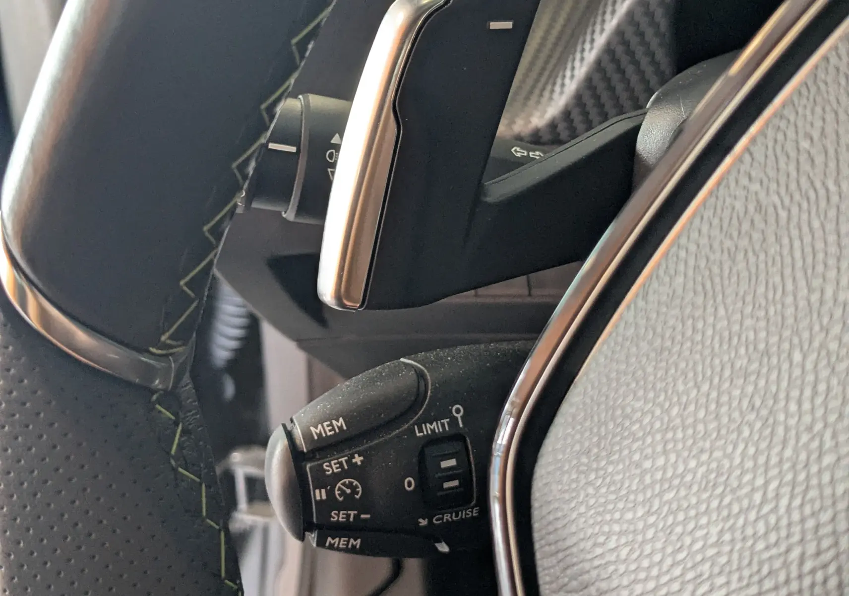 Gros plan sur la commande de régulateur de vitesse au volant noir avec surpiqûres vertes du Peugeot 208 Hybrid 145 e-DCS6 GT.