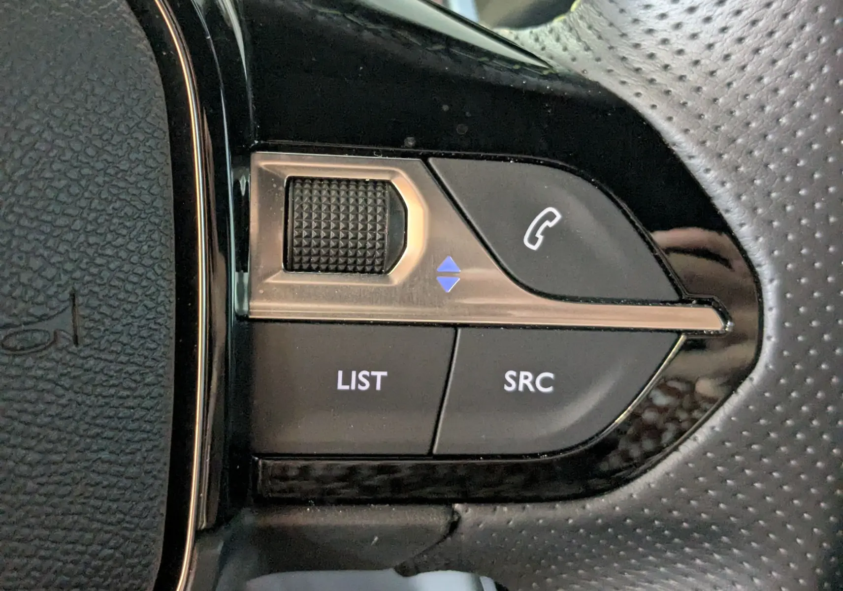 Gros plan sur les commandes multifonctions du volant perforé noir de la Peugeot 208 Hybrid 145 e-DCS6 GT 2025.