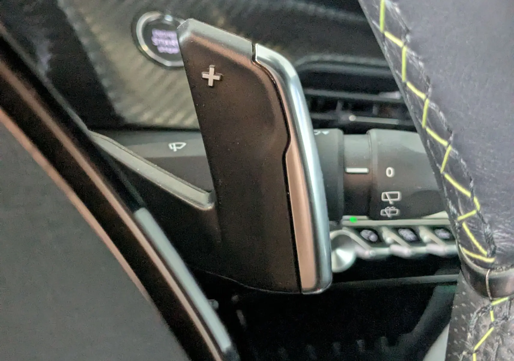 Gros plan sur la palette de changement de vitesse "+" côté droit du volant avec surpiqûres vertes dans un Peugeot 208 gris Selenium.
