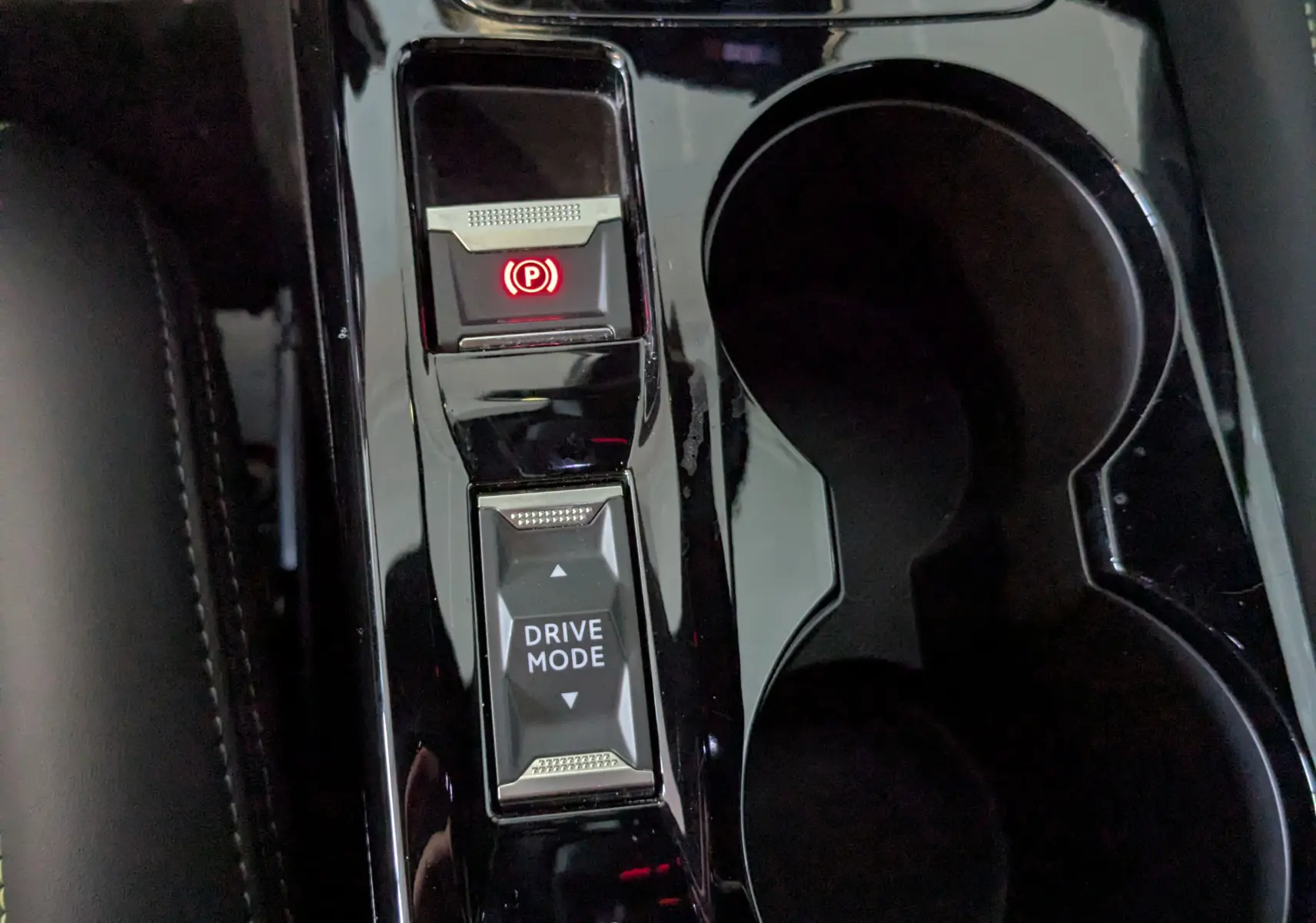 Gros plan sur la console centrale noire brillante de la Peugeot 208 Hybrid 145 e-DCS6 GT avec bouton frein à main électronique et mode de conduite.