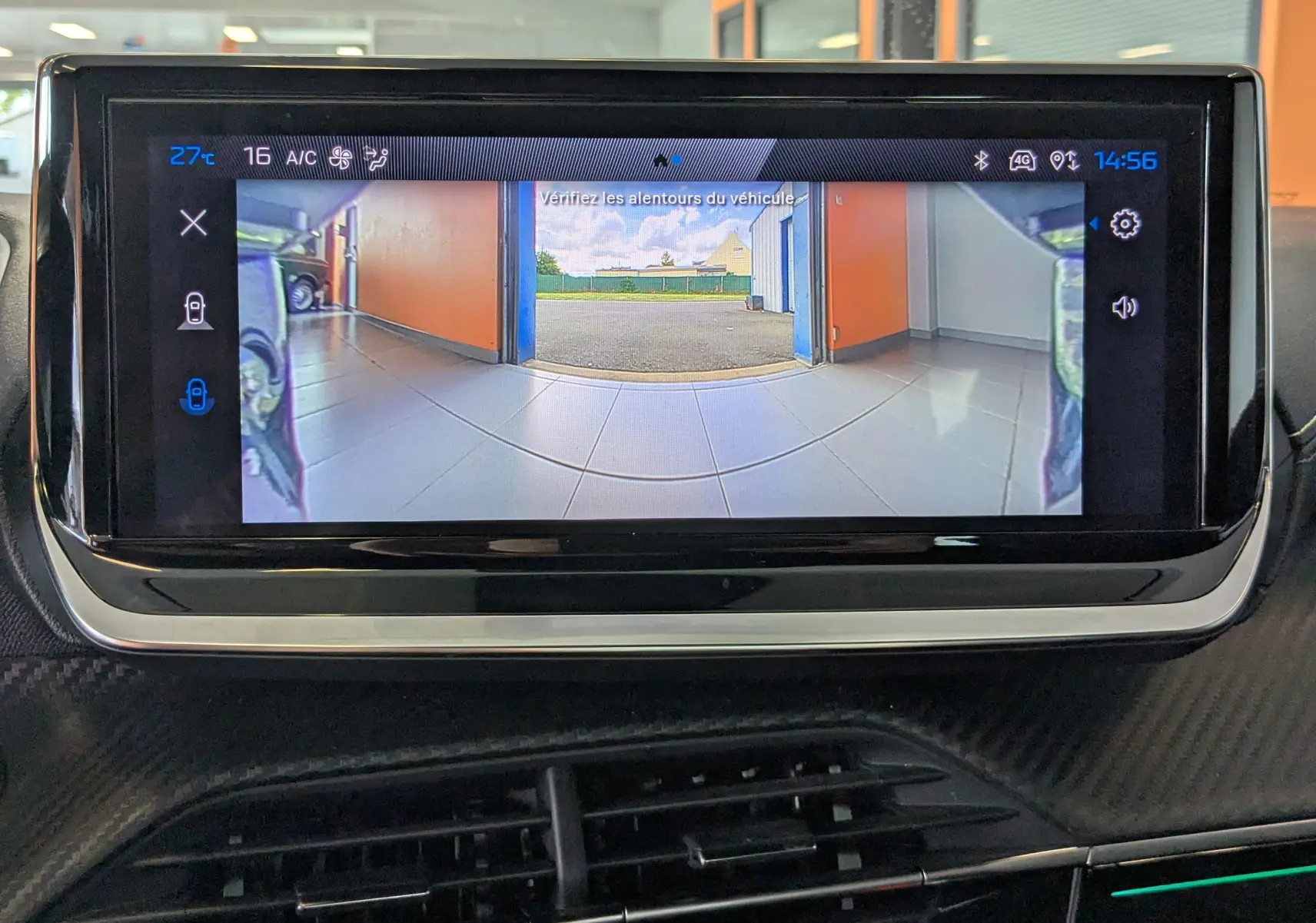 Écran tactile intérieur montrant la caméra de recul du Peugeot 208 gris Selenium avec vue arrière sur un garage.