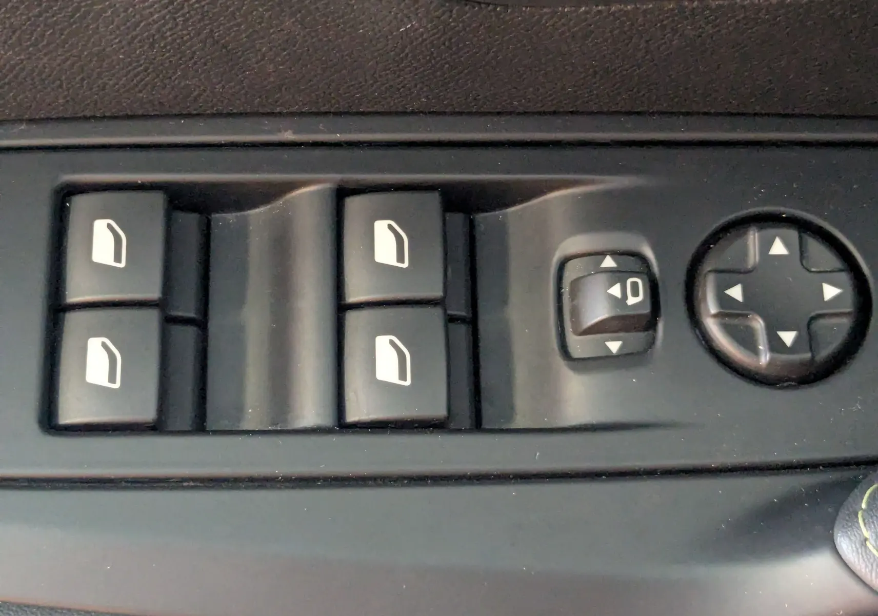 Gros plan sur les commandes de lève-vitres et réglage des rétroviseurs côté conducteur d’une Peugeot 208 gris Selenium.