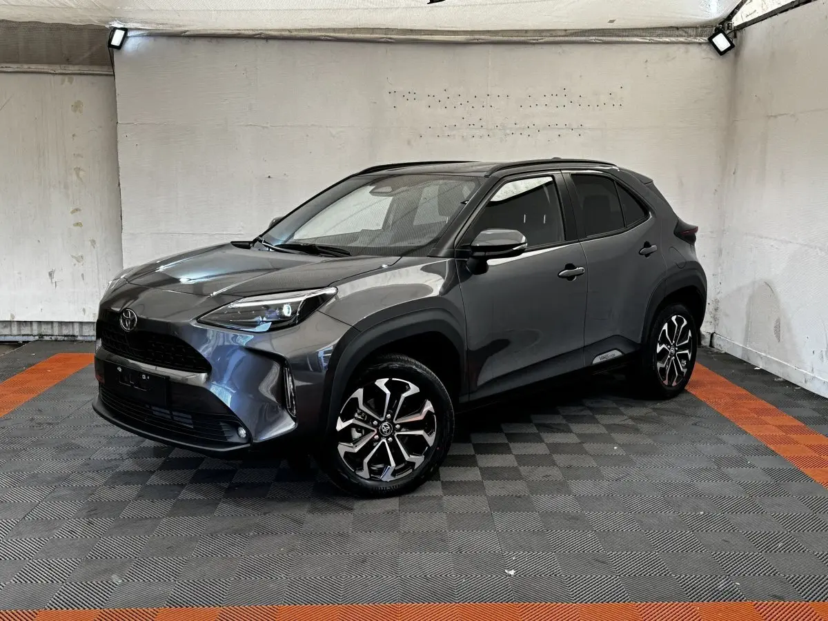 Toyota Yaris Cross 2026 gris foncé vue 3/4 avant avec jantes alliage et toit noir dans un garage.
