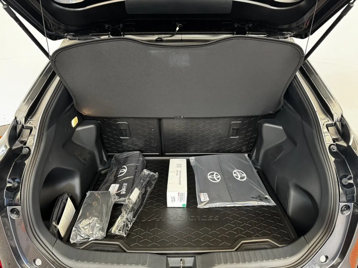 Coffre ouvert d’une Toyota Yaris Cross gris foncé, vue arrière, avec accessoires d’origine posés à l’intérieur.