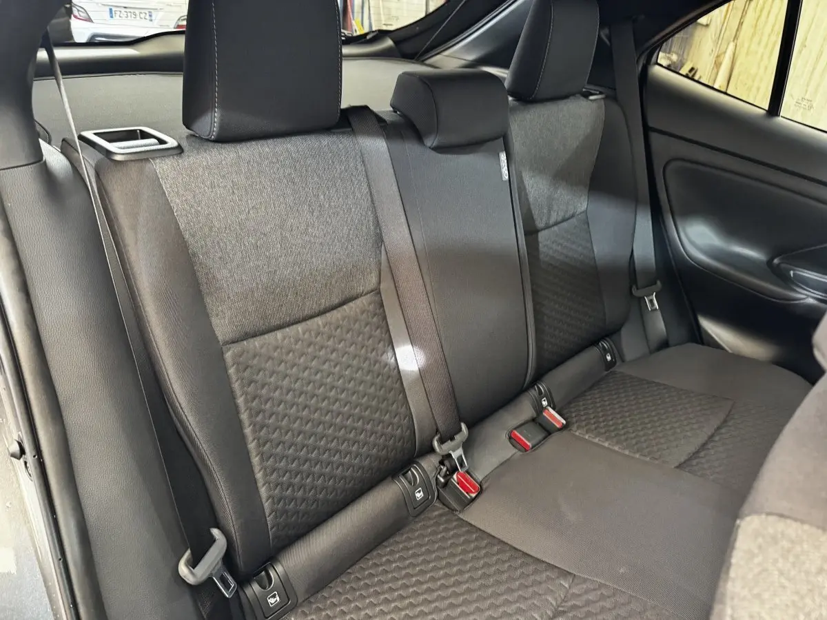 Vue intérieure de la banquette arrière grise foncée de la Toyota Yaris Cross 1.5 Hybrid 130h Design Auto, avec ceintures et appuie-têtes.