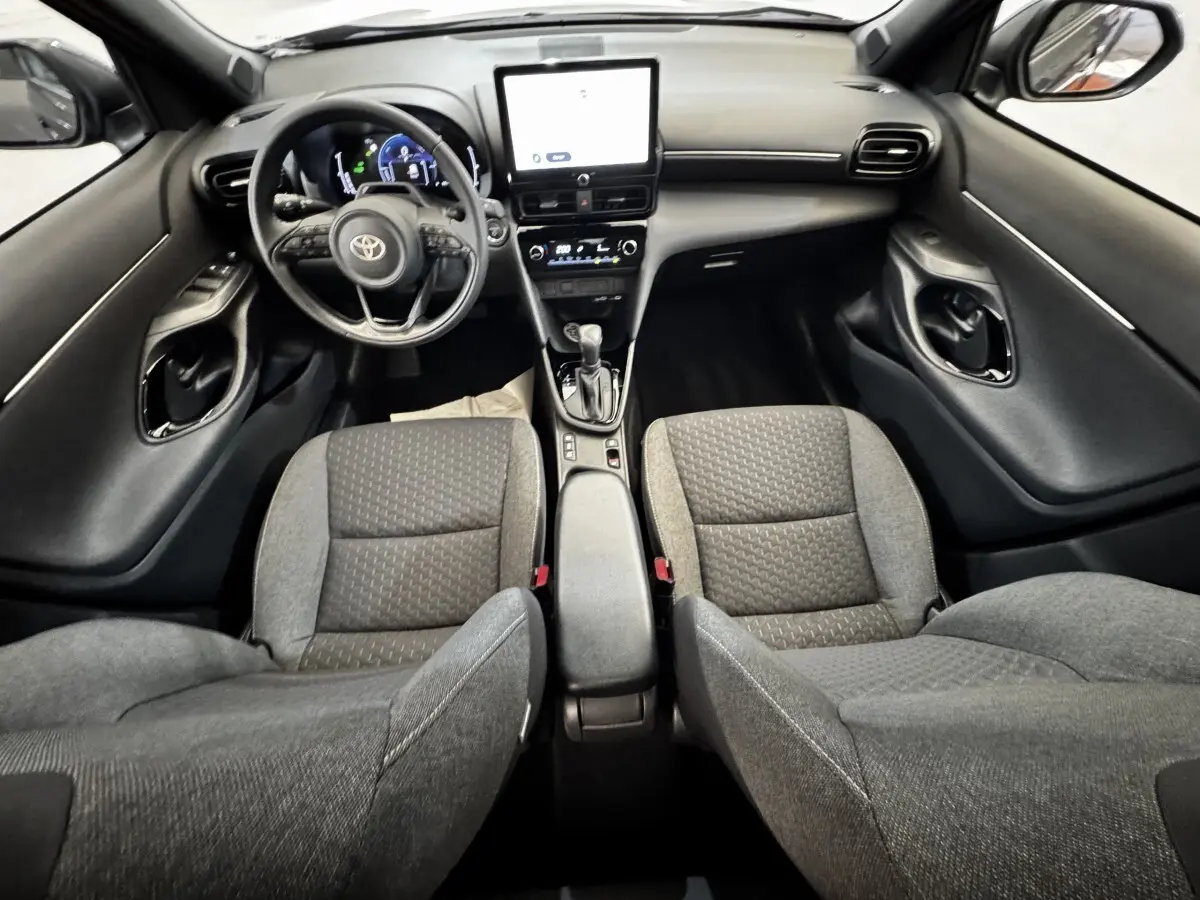 Vue intérieure avant de la Toyota Yaris Cross 1.5 Hybrid 130h, sièges gris et tableau de bord avec écran tactile central.