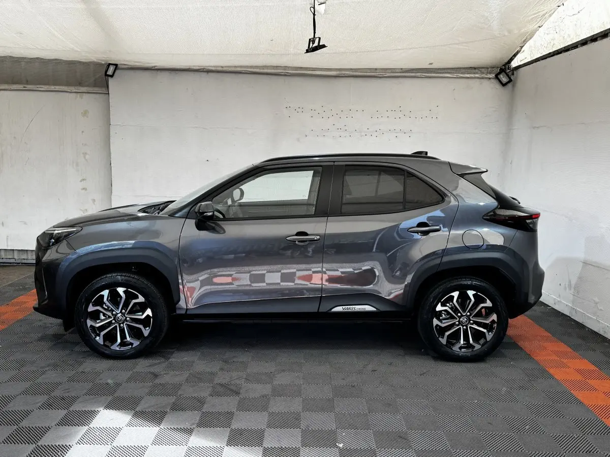 Profil droit de la Toyota Yaris Cross 2026 gris foncé avec jantes alliage et protections noires sur les passages de roues.