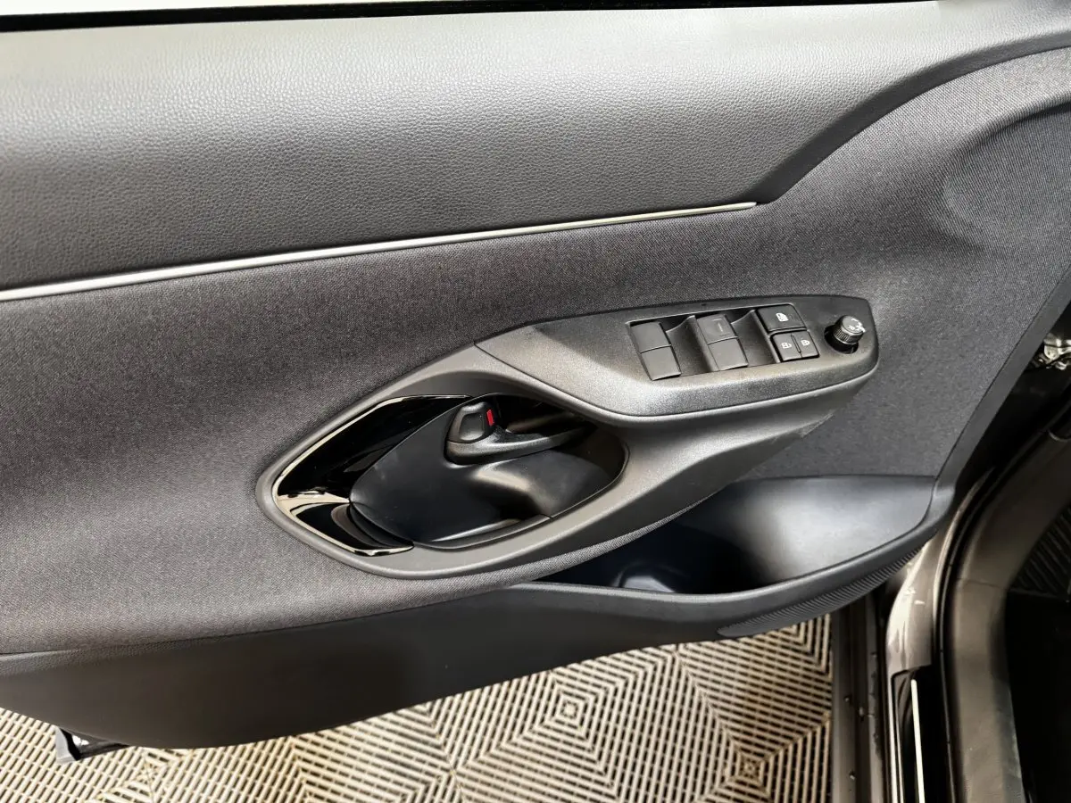 Gros plan sur la porte avant gauche de la Toyota Yaris Cross 2026 gris foncé, montrant les commandes des vitres et la poignée intérieure.