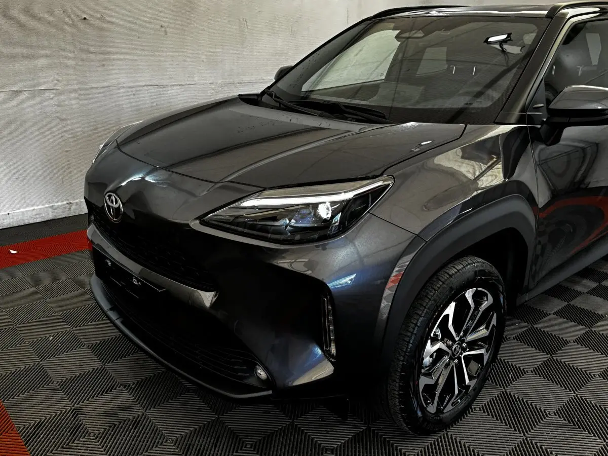 Vue 3/4 avant droit d'une Toyota Yaris Cross 1.5 Hybrid 130h gris foncé avec jantes alliage et phares LED allumés.