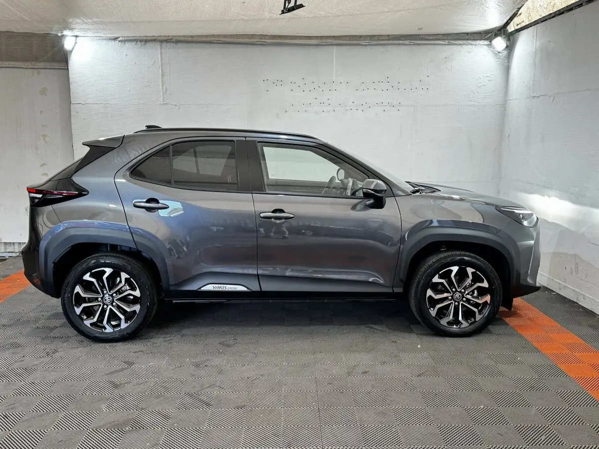 Vue de profil droit d'un Toyota Yaris Cross gris foncé avec jantes alliage bicolores et protections noires sur les passages de roues.