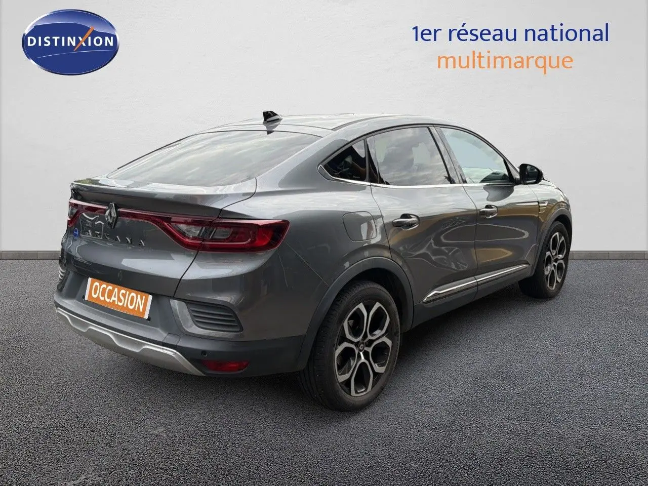 Renault Arkana gris en 3/4 arrière droit, avec feux LED et jantes bi-ton distinctives sur sol gris.