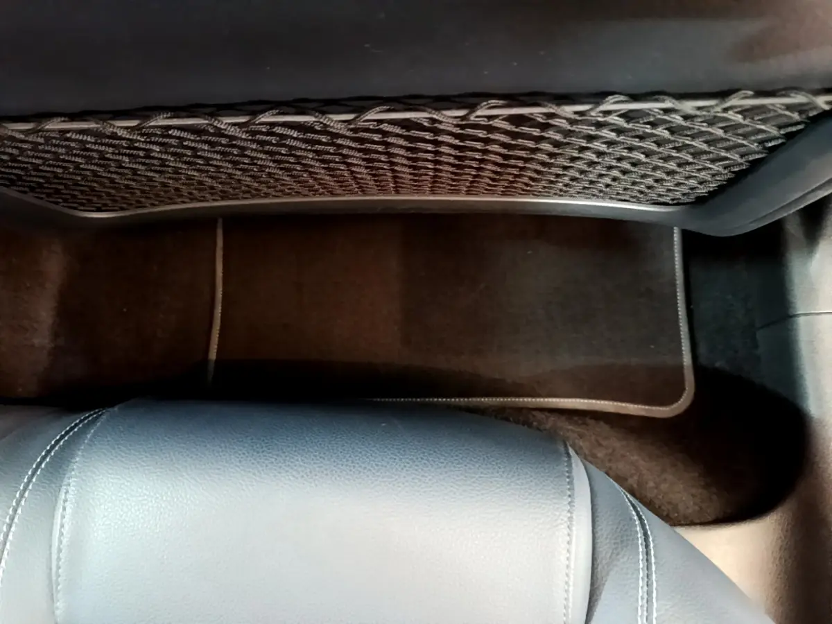 Vue intérieure du plancher arrière avec tapis noir et filet de rangement sur le dossier du siège avant d'une Mercedes Classe A gris clair.