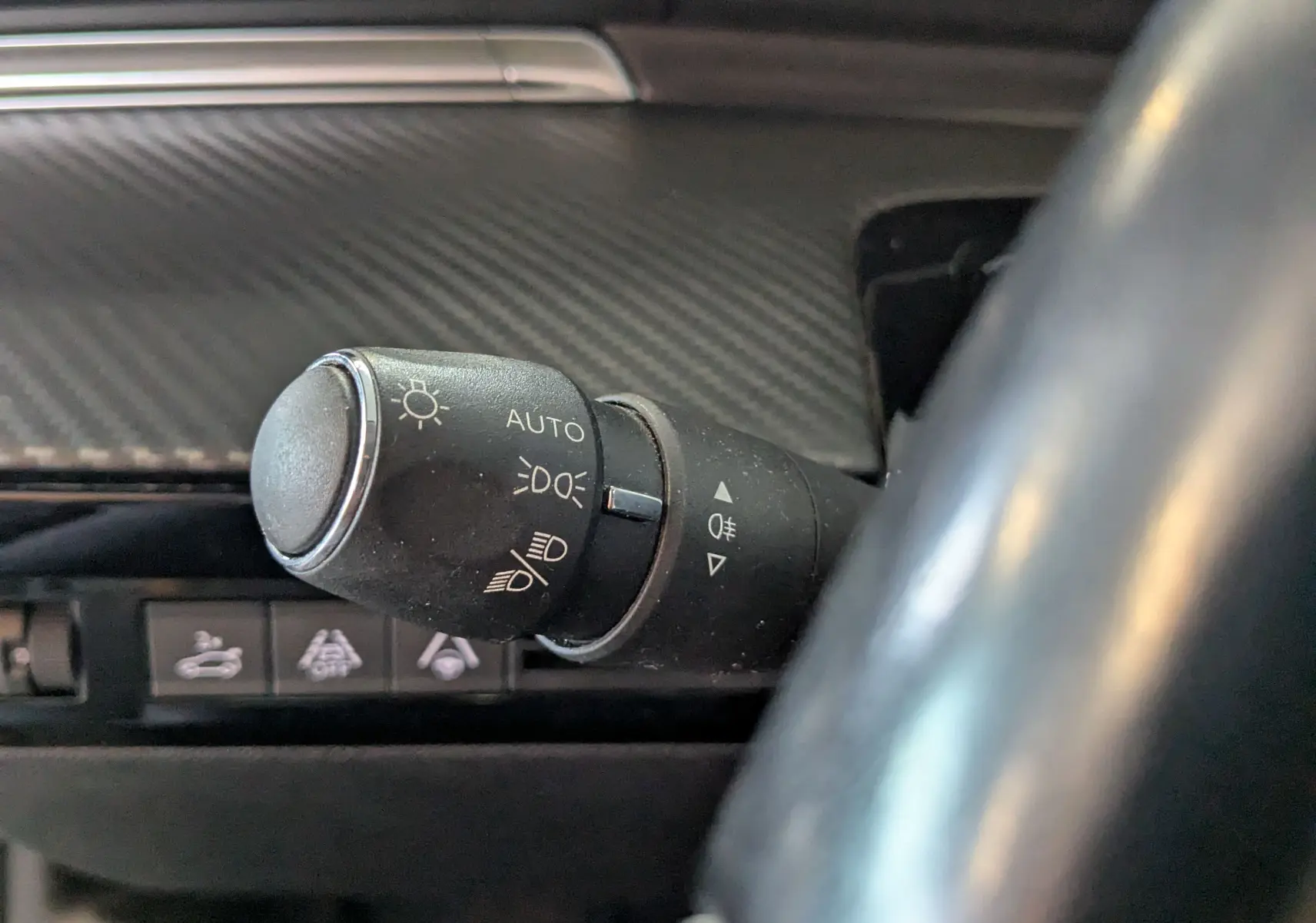 Gros plan sur la commande des phares à gauche du volant dans l’habitacle gris carbone d’une Peugeot 508 SW 2021.