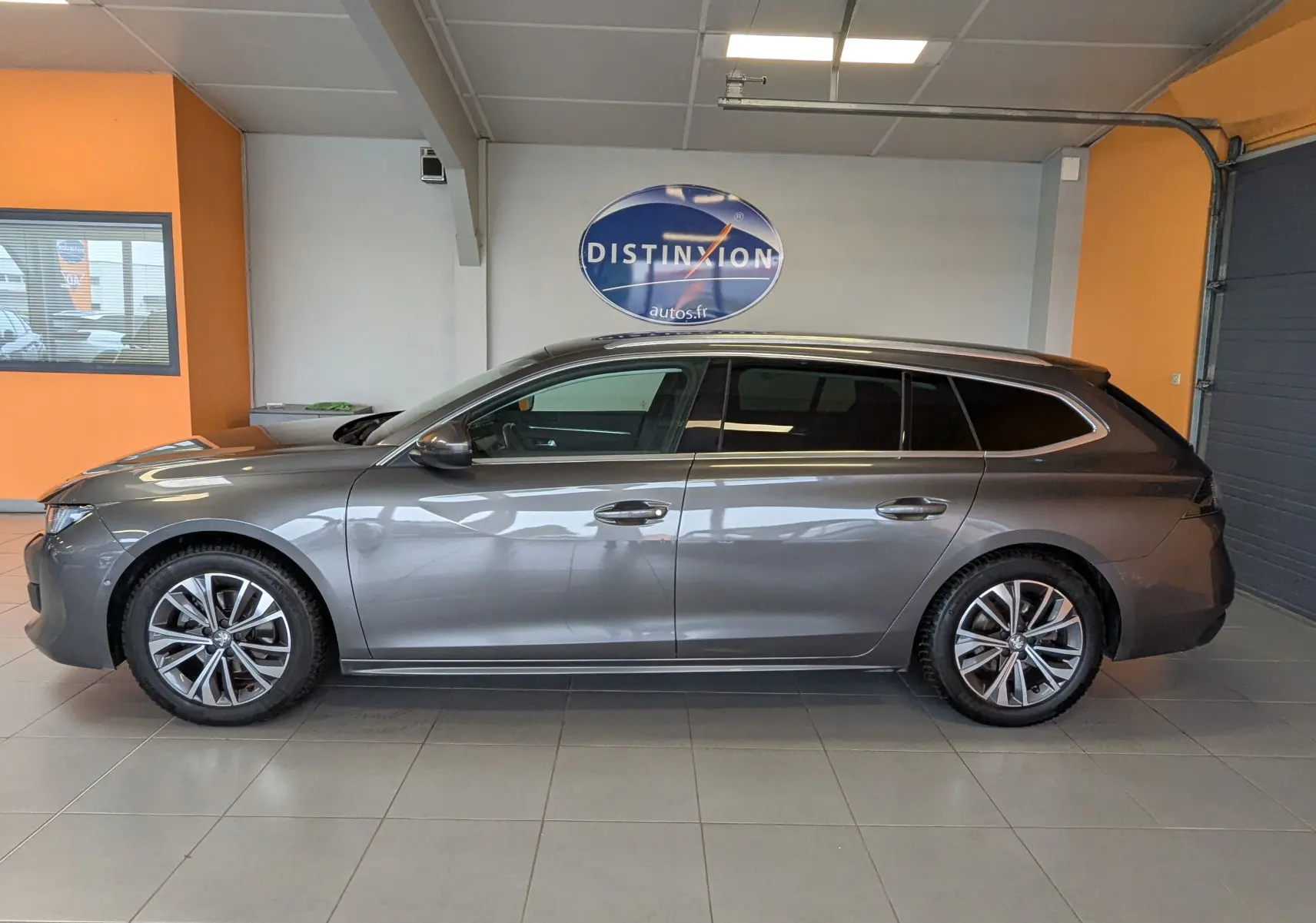 Vue de profil côté gauche d'une Peugeot 508 SW gris métallisé 2021 en intérieur, avec jantes bi-ton et vitres teintées.