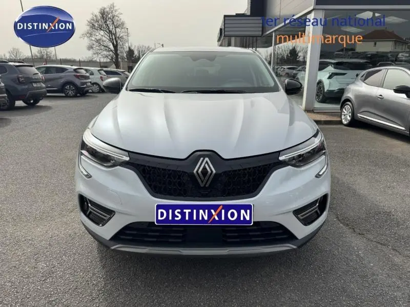 Vue frontale d'un Renault Arkana blanc 2025 avec calandre noire et logo Renault bien visible sur un parking extérieur.