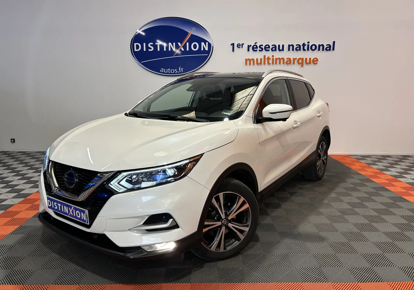 Nissan Qashqai blanc en 3/4 avant droit, avec toit panoramique et jantes alliage bicolores visibles.