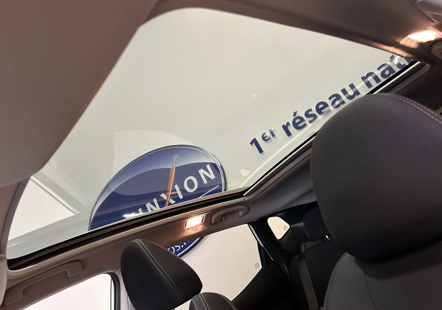 Vue intérieure du toit panoramique ouvert du Nissan Qashqai blanc, mettant en valeur les sièges avant en tissu noir.