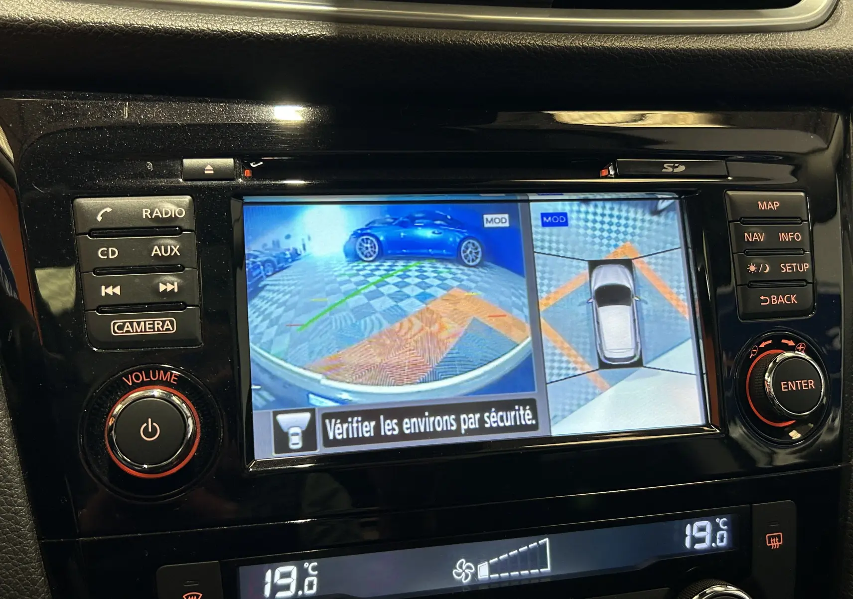 Écran central du Nissan Qashqai blanc montrant la caméra 360° avec vue arrière et vue aérienne du véhicule.