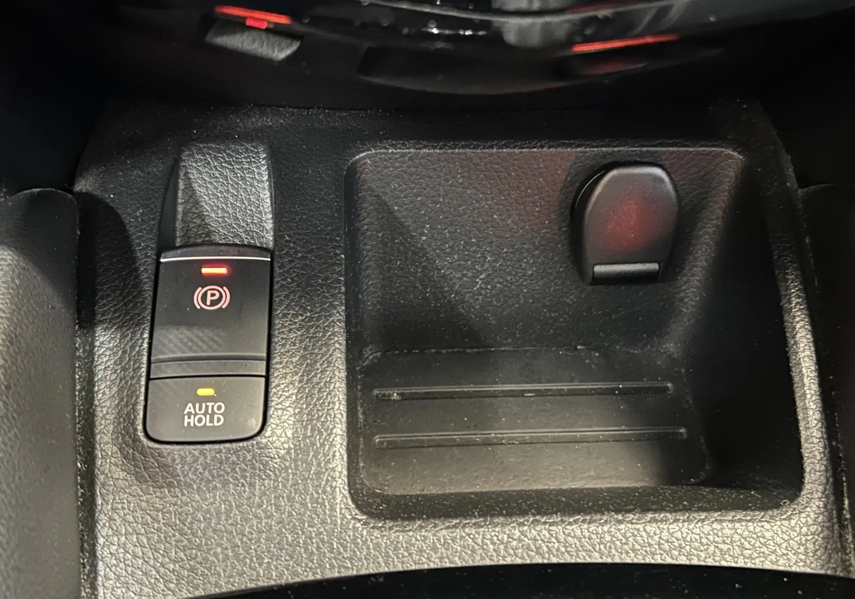 Gros plan sur la console centrale noire du Nissan Qashqai 1.6 dCi avec bouton frein à main électronique et rangement.