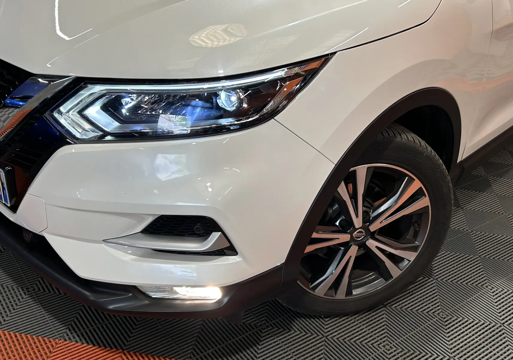Gros plan sur l'avant droit blanc du Nissan Qashqai 2018, mettant en valeur le phare LED et la jante alliage bicolore.