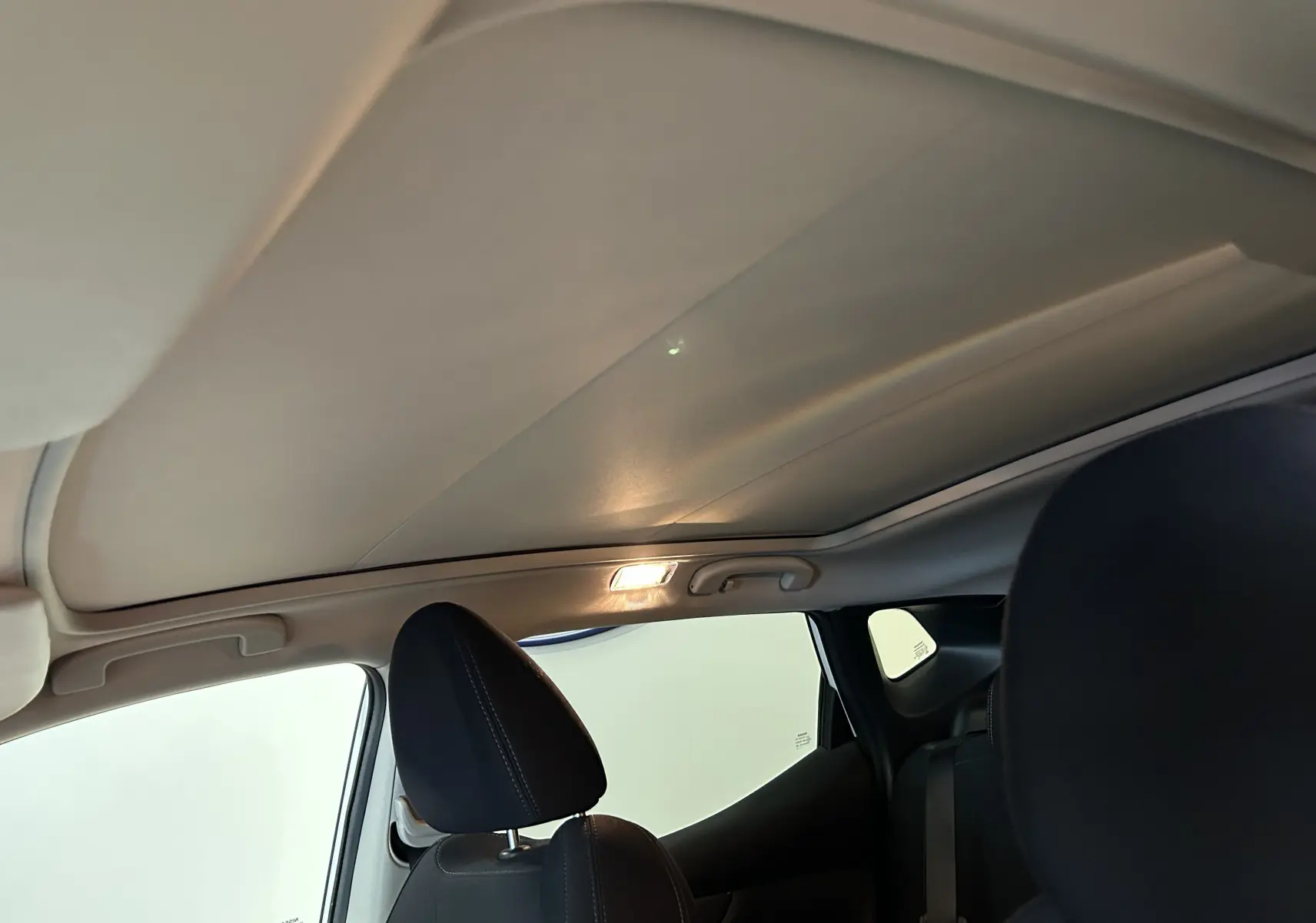 Vue intérieure du toit panoramique fermé et des appuie-têtes noirs du Nissan Qashqai blanc, version 2018.