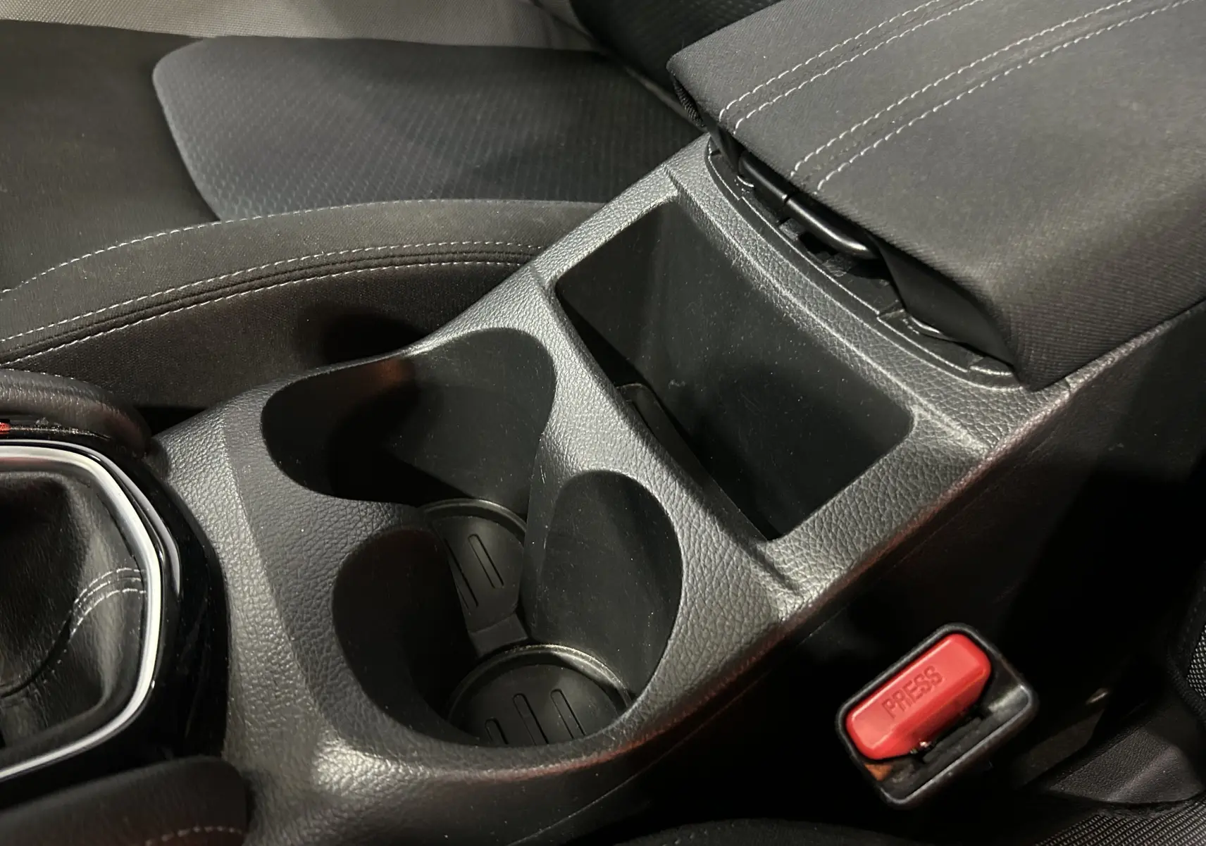Gros plan sur la console centrale noire avec porte-gobelets et bouton de ceinture rouge dans un Nissan Qashqai 2018.