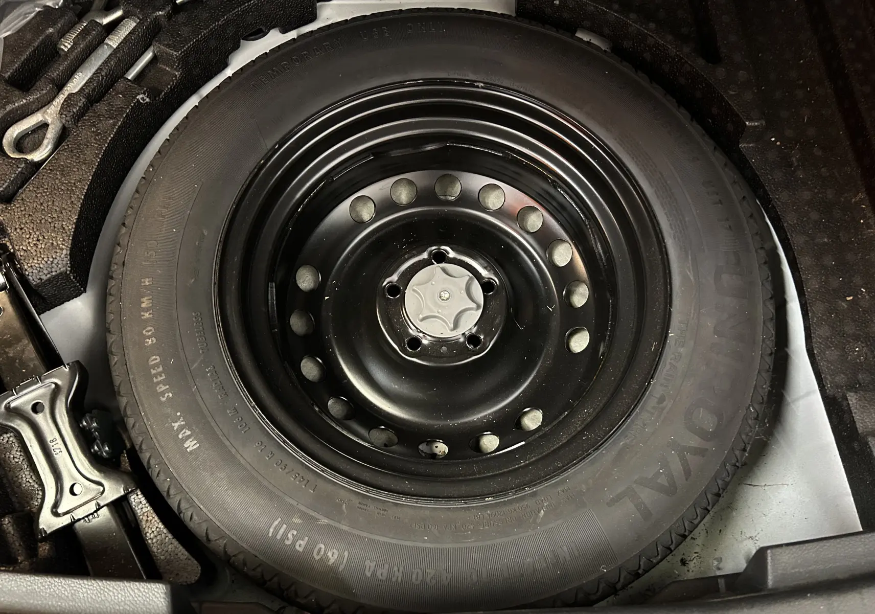 Gros plan sur la roue de secours noire en acier du Nissan Qashqai blanc, visible dans le coffre.