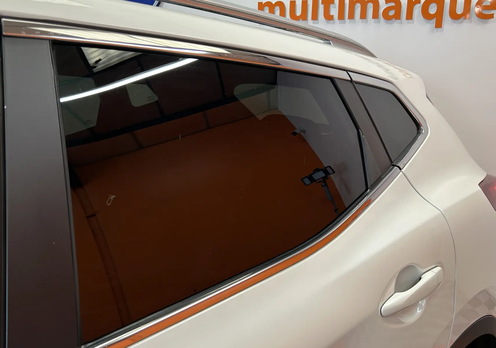 Vue rapprochée du côté arrière droit d’un Nissan Qashqai blanc avec vitrage teinté et poignée de porte visible.