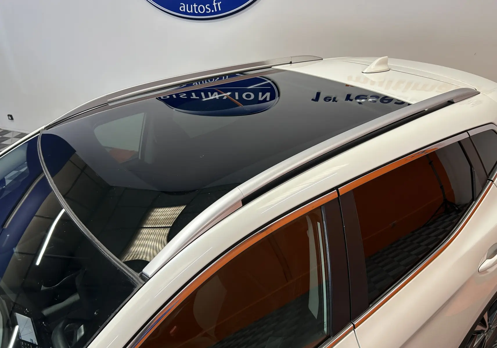 Vue plongeante du toit panoramique noir sur Nissan Qashqai blanc, avec barres de toit argentées et vitres teintées.