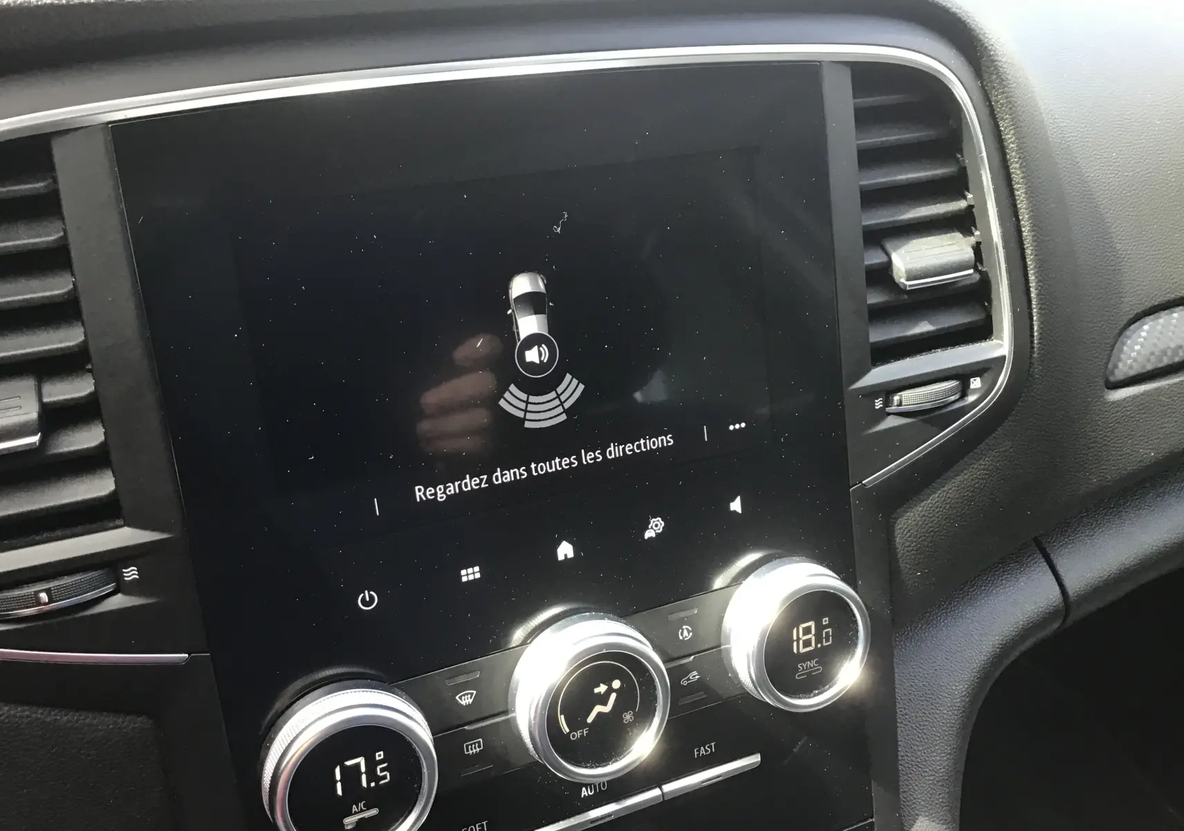 Vue rapprochée de la console centrale noire de la Renault Mégane IV Société blanche, avec écran tactile et commandes de climatisation.