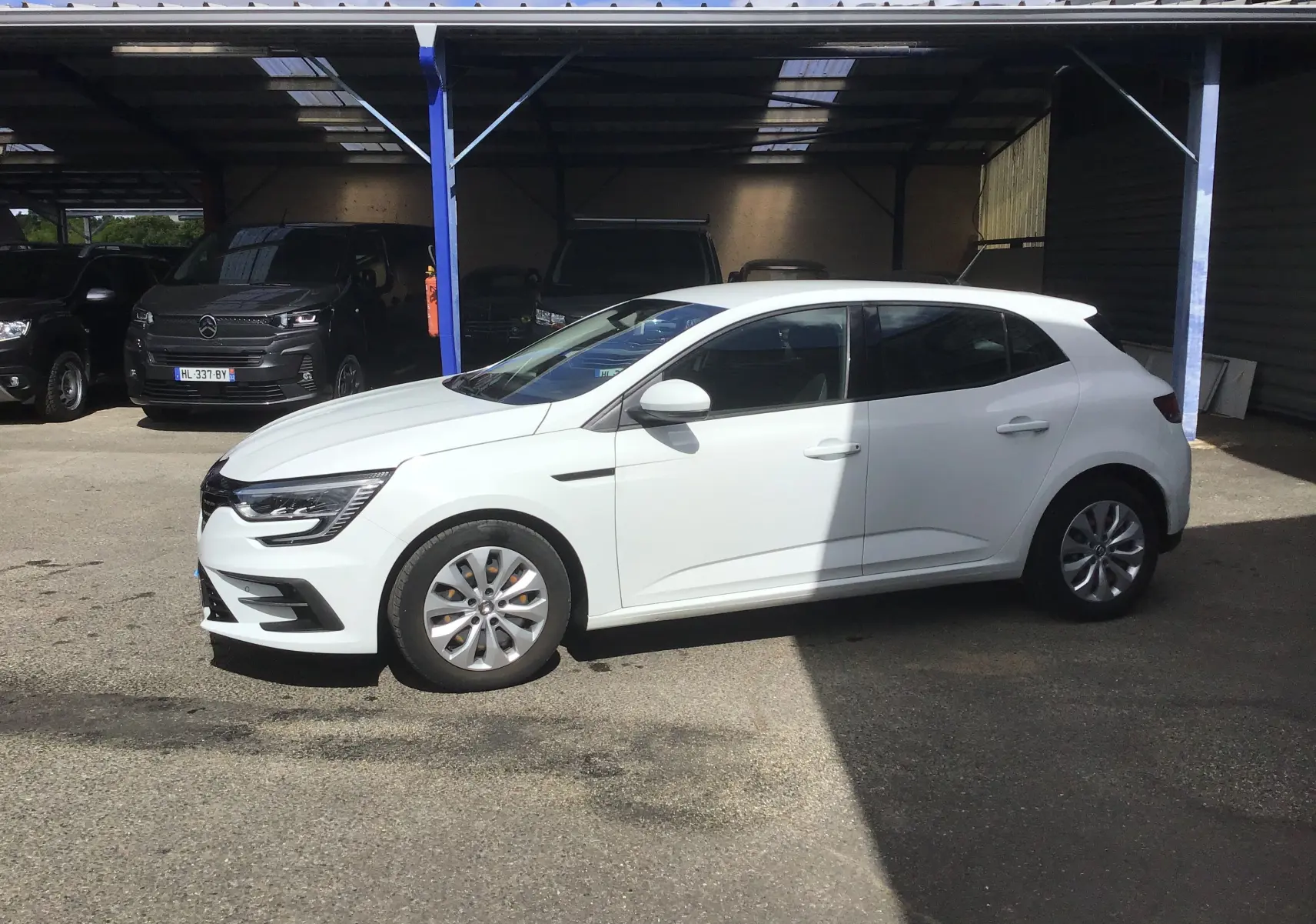 Renault Mégane IV Société blanche vue de profil côté gauche, stationnée à l'extérieur sous un abri partiel.