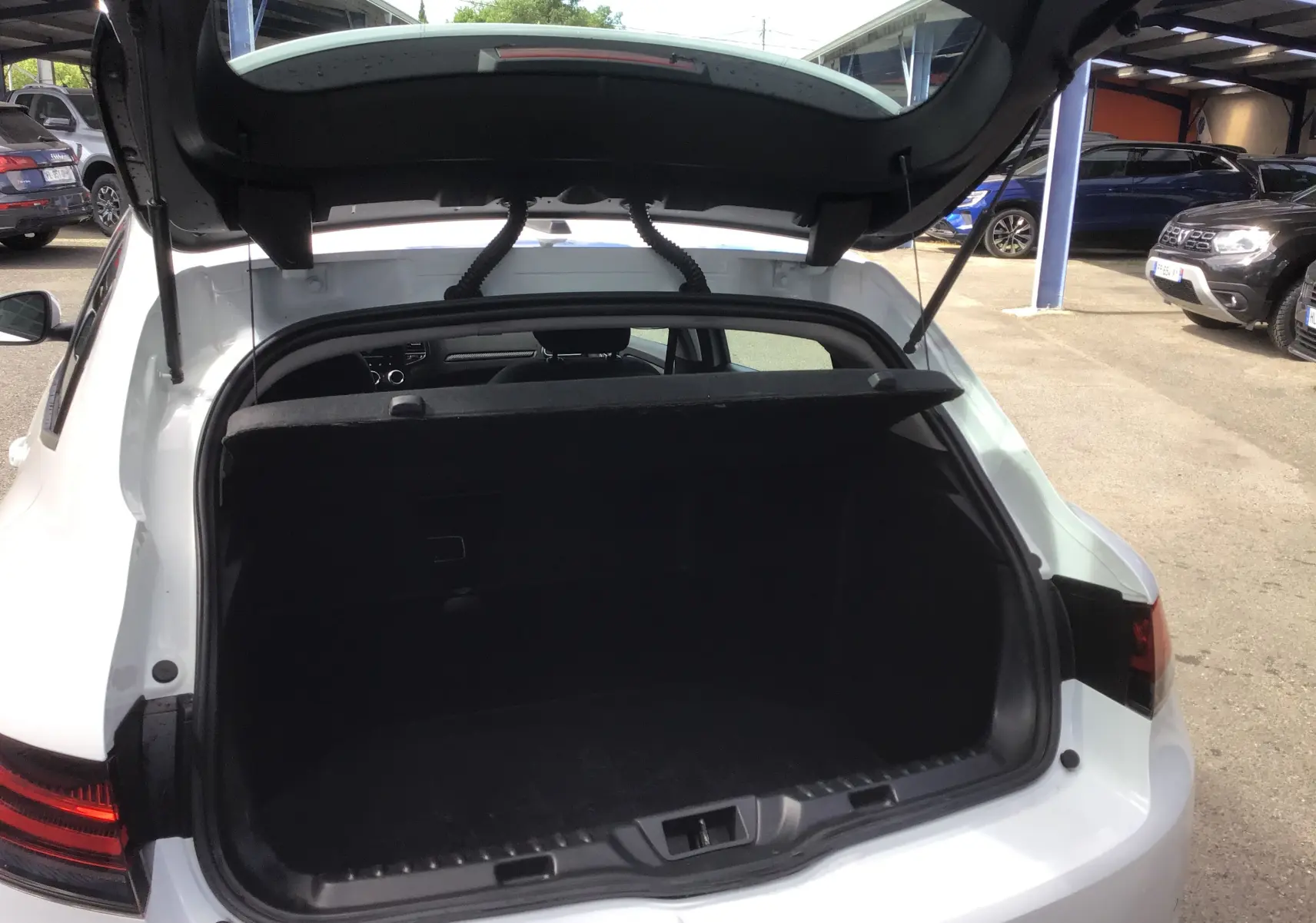 Coffre ouvert vu de l'arrière d'une Renault Mégane IV Société blanche, montrant l'espace de chargement vide.