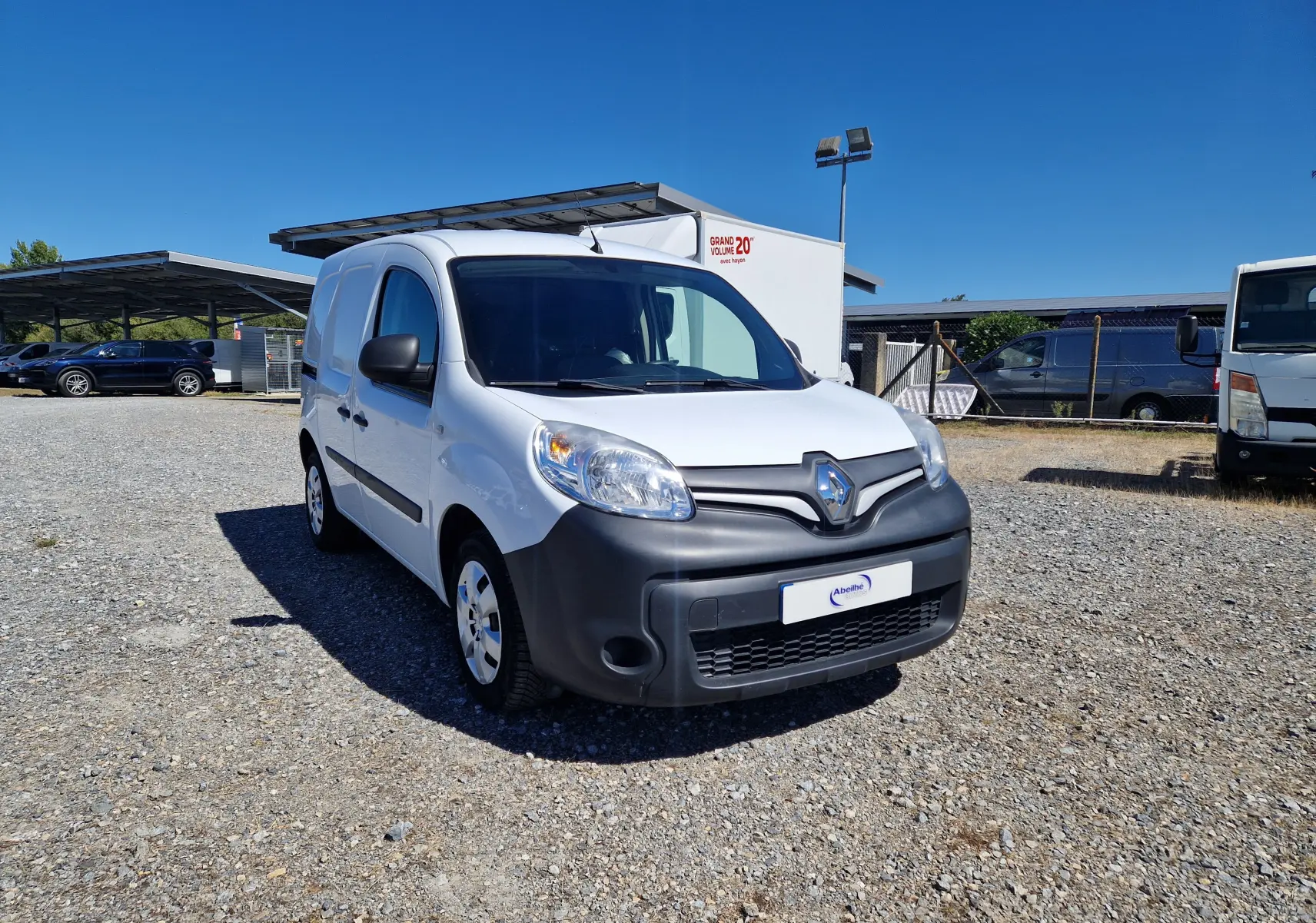 Renault Kangoo blanc vue 3/4 avant droit avec pare-chocs noir mat sur un parking en extérieur.