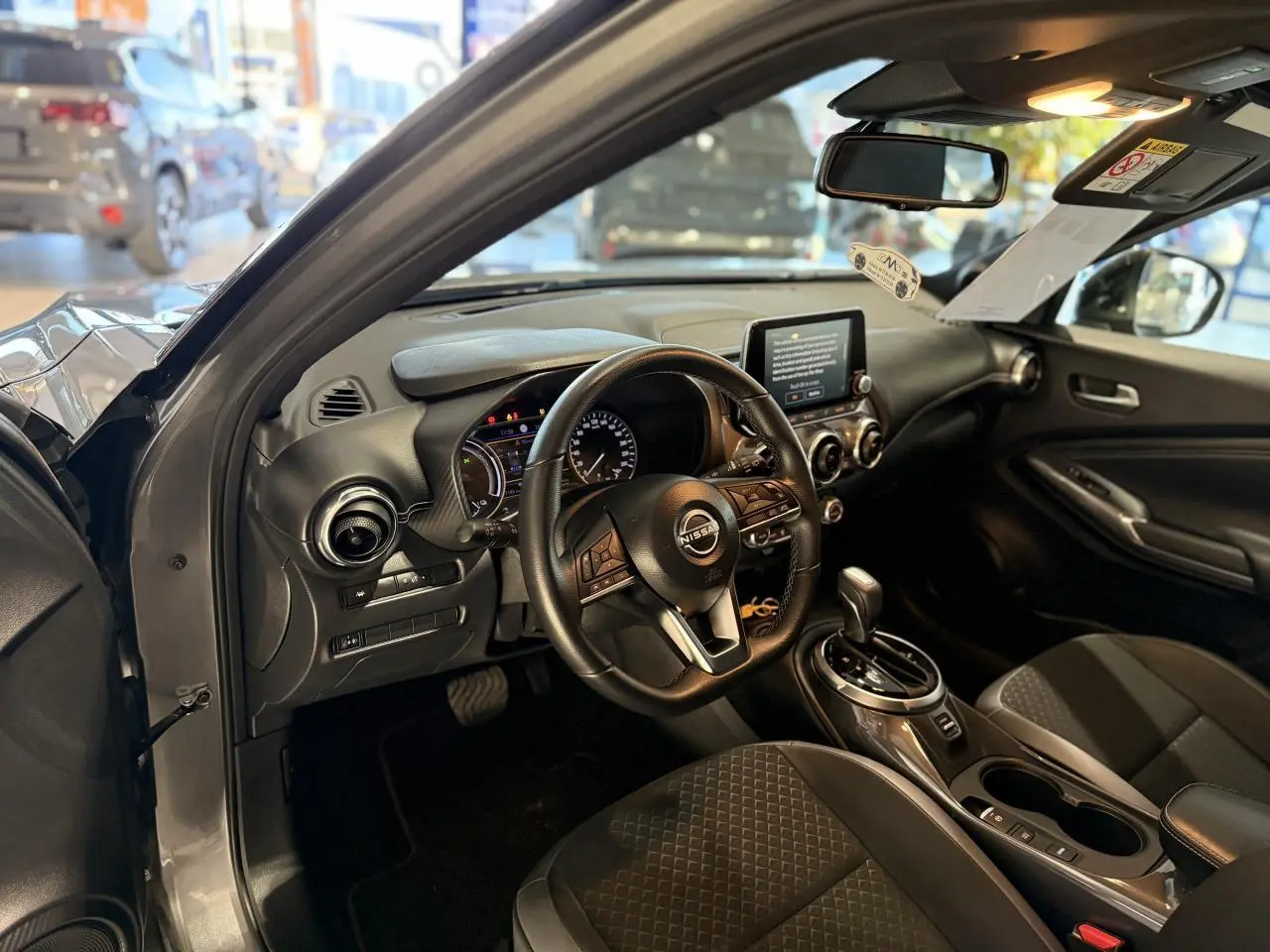 Intérieur du Nissan Juke Hybrid 2024 vu côté conducteur, avec tableau de bord noir et volant multifonction cuir.