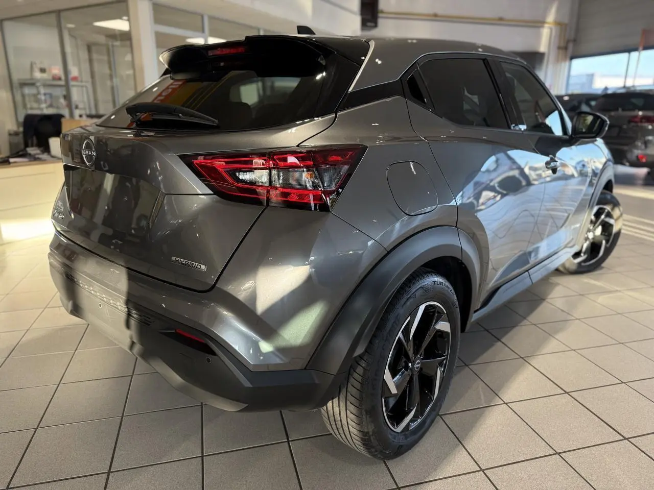 Vue 3/4 arrière droit du Nissan Juke Hybrid gris métallisé avec jantes alliage noires en showroom.