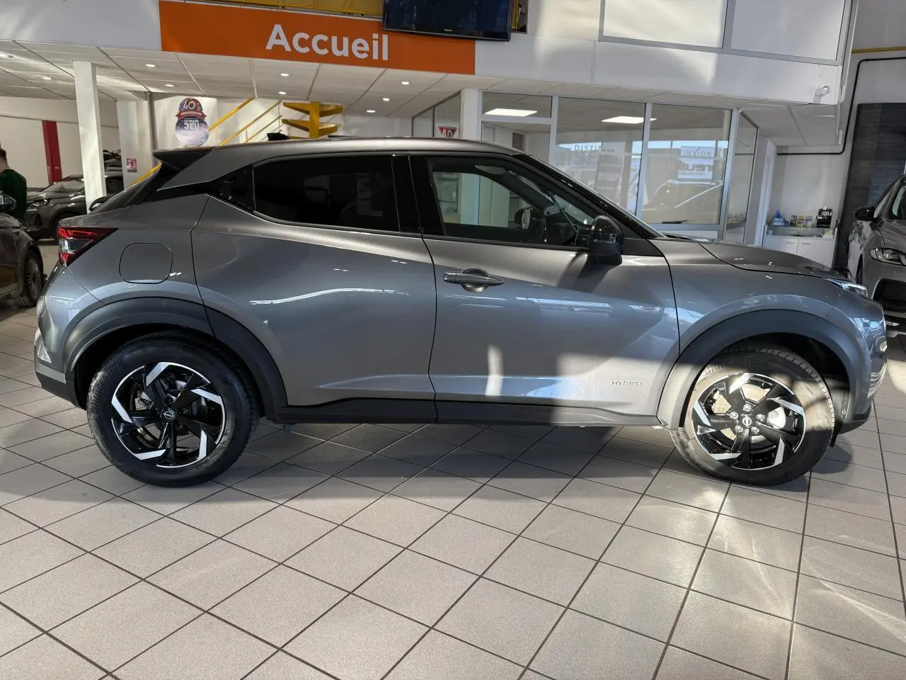 Profil côté gauche du Nissan Juke Hybrid 143 N-Connecta gris métallisé en showroom avec jantes alliage noires et chromées.