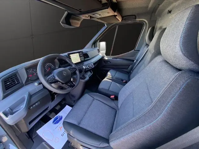 Vue intérieure côté conducteur du Renault Master 2025, montrant les sièges gris chiné avec surpiqûres bleues et le tableau de bord moderne.