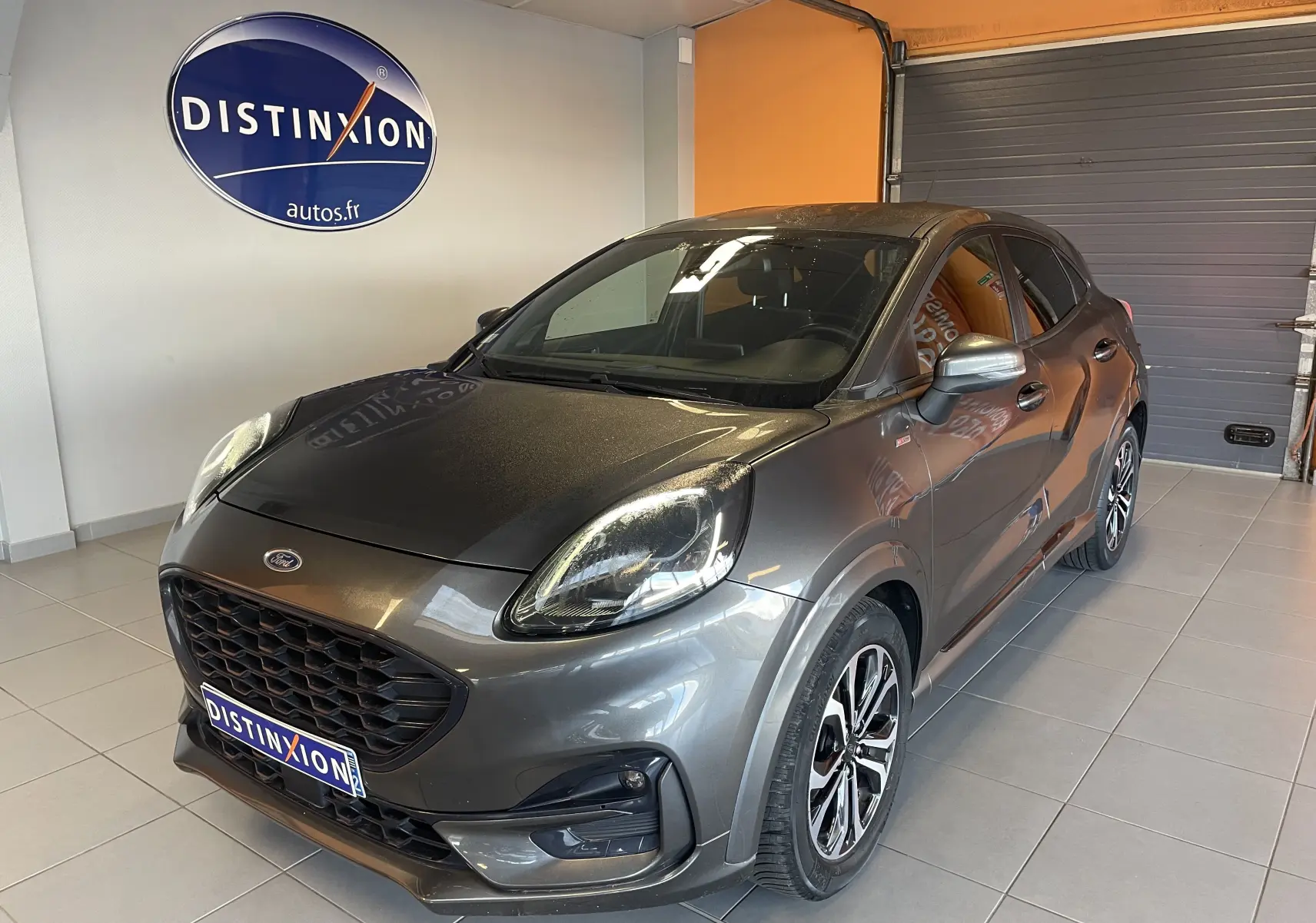 Vue 3/4 avant d'une Ford Puma gris métallisé 2020 en finition ST Line, avec jantes alliage et calandre noire en showroom.