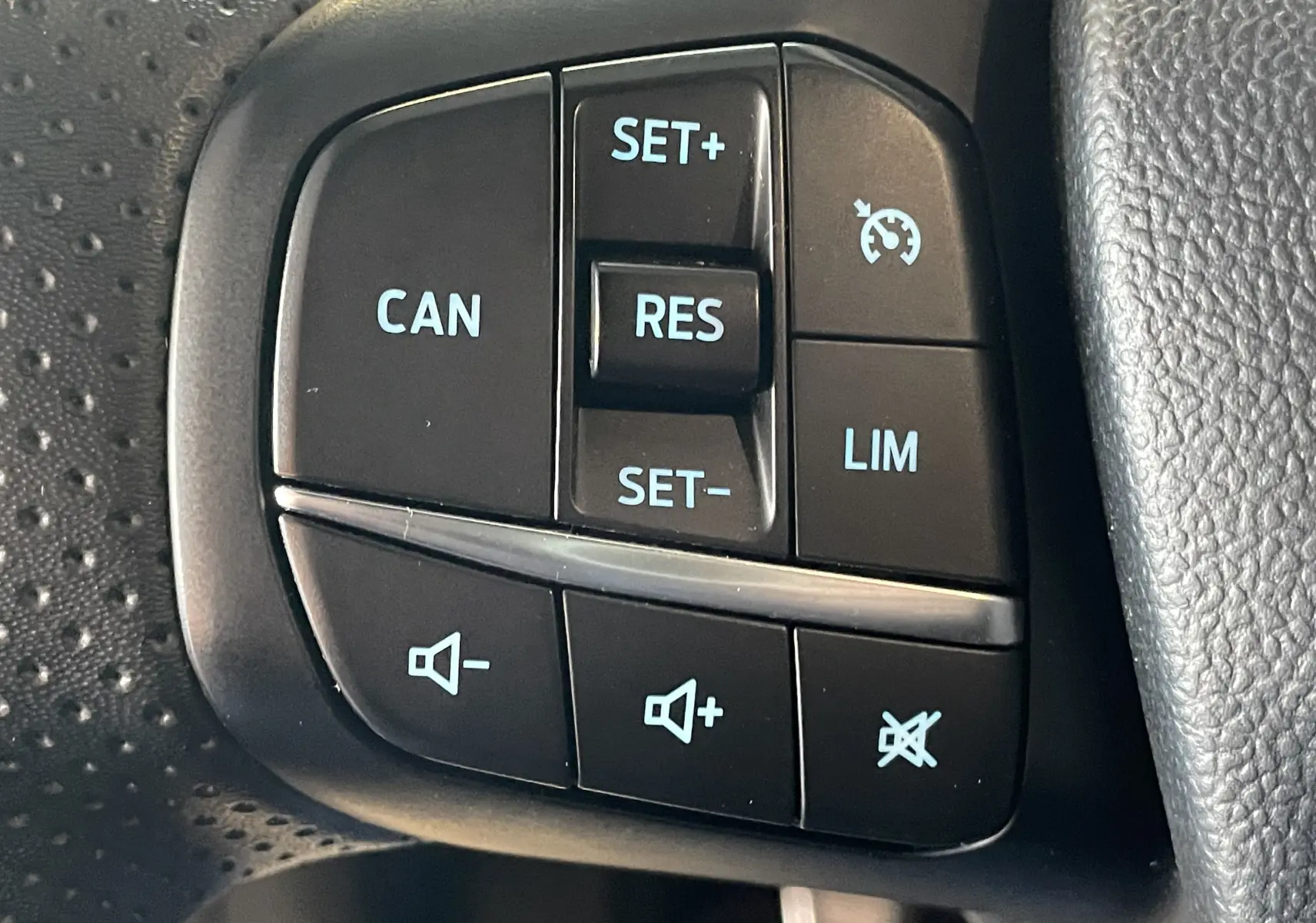 Gros plan sur les commandes au volant noir du Ford Puma gris 2020, avec boutons de régulateur de vitesse et volume sonore.