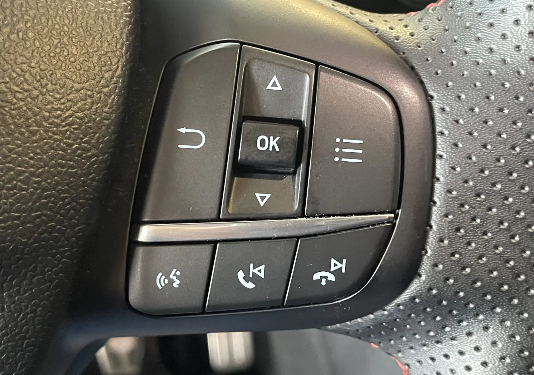 Gros plan sur les commandes multifonctions noires du volant perforé avec surpiqûres rouges du Ford Puma gris 2020.