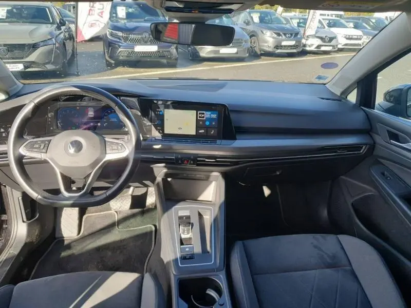 Intérieur noir de la Volkswagen Golf 1.5 eTSI 2021, vue du poste de conduite avec écran tactile et volant multifonction.