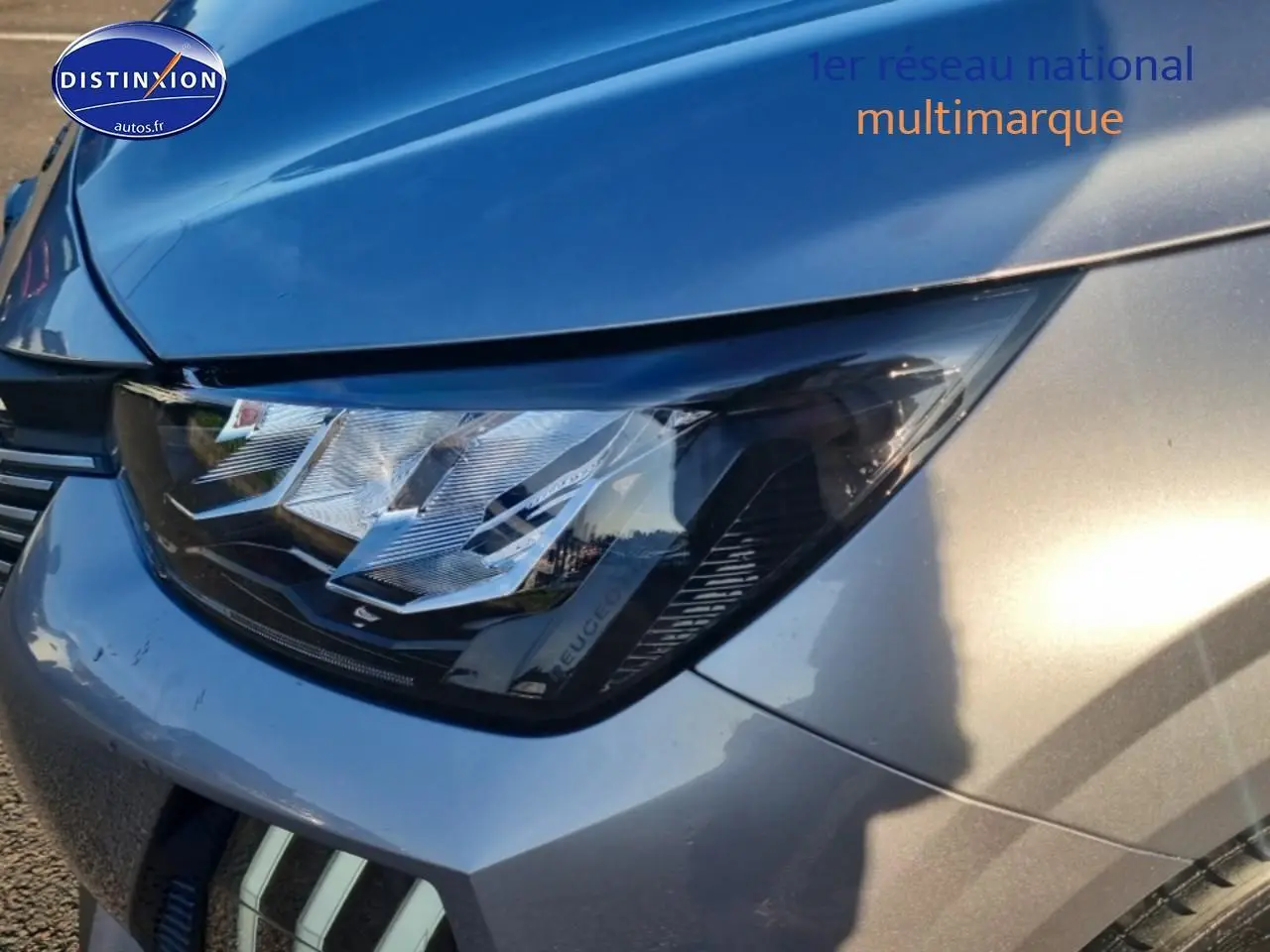 Gros plan sur le phare avant droit d'une Peugeot 208 gris artense avec reflets métalliques.