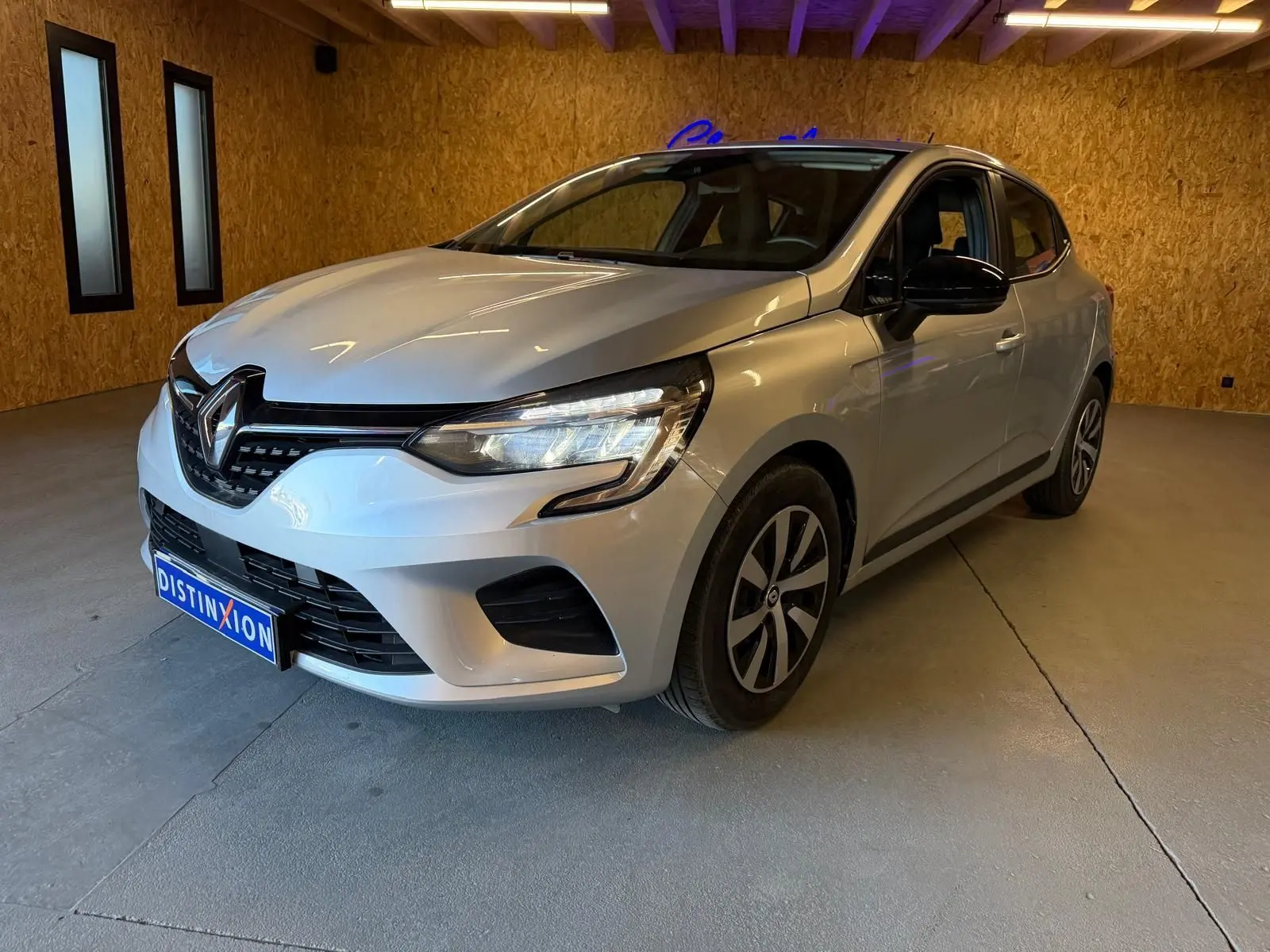 Renault Clio gris platine vue 3/4 avant droit, avec phares LED et jantes alliage distinctives.