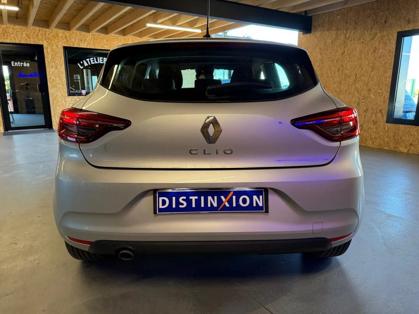 Vue arrière d'une Renault Clio gris platine 2023 avec feux arrière LED et becquet, en intérieur showroom.
