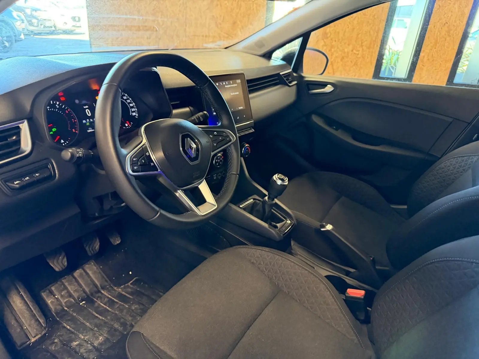 Vue intérieure côté conducteur de la Renault Clio gris platine 2023, volant multifonction et écran tactile central visible.