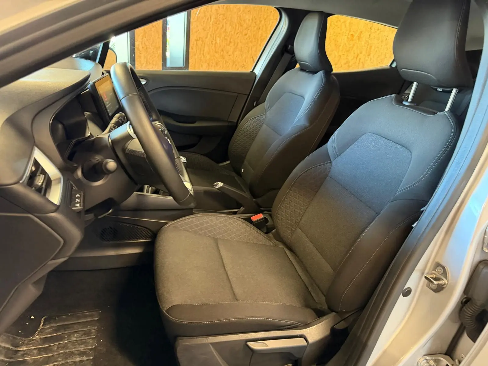 Vue intérieure côté conducteur de la Renault Clio 1.0 TCE 90 Équilibre 2023 avec sièges tissu gris et volant réglable.